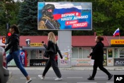 People walk past a billboard displaying a soldier and a Russian flag and reading "We believe in our army and our victory," in Luhansk, Luhansk People's Republic controlled by Russia-backed separatists, eastern Ukraine, Sept. 27, 2022.