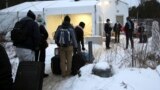 FILE - Migrants line up on the border of the United States, foreground, and Canada, background, at a reception center for irregular borders crossers, in Saint-Bernard-de-Lacolle, Quebec, Canada, Jan. 12, 2022, in a photo taken from Champlain, New York. 
