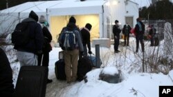 FILE - Migrants line up on the border of the United States, foreground, and Canada, background, at a reception center for irregular borders crossers, in Saint-Bernard-de-Lacolle, Quebec, Canada, Jan. 12, 2022, in a photo taken from Champlain, New York. 