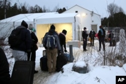 FILE - Migrants line up on the border of the United States, foreground, and Canada, background, at a reception center for irregular borders crossers, in Saint-Bernard-de-Lacolle, Quebec, Canada, Jan. 12, 2022, in a photo taken from Champlain, New York.
