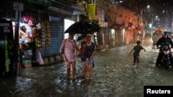 People wade through a flooded street in continuous rain in Dhaka, Bangladesh, October 24, 2022, before Cyclone Sitrang hits the country.
