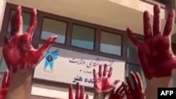 This image grab from a UGC video made available on Twitter Oct. 9, 2022, shows Iranian students from the Faculty of Arts at Tehran's Azad University participating in a protest with their palms covered in red paint to symbolize blood.