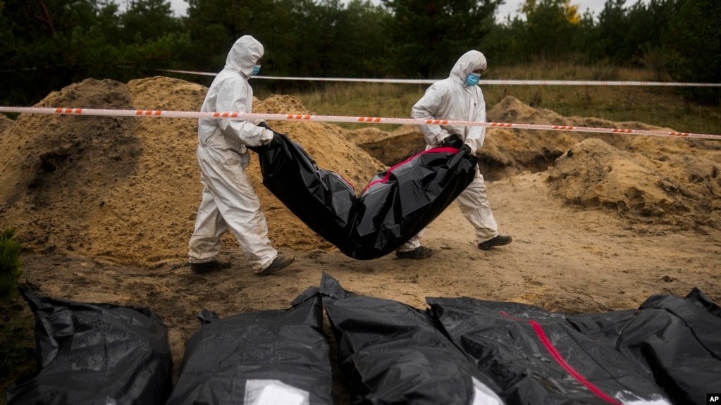 资料照片：司法鉴定组成员在乌克兰莱曼的群葬坑中抬起一个装有尸体的塑料袋。(2022年10月11日)