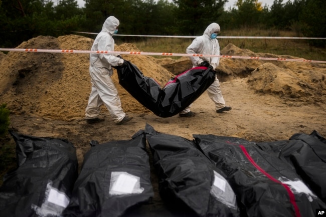 Members of a forensic team carry a plastic bag with a body inside as they work in an exhumation in a mass grave in Lyman, Ukraine, Oct. 11, 2022.