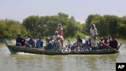 FILE - Villagers with their belongings cross a flooded area on a boat, in Dadu, a district of southern Sindh province, Pakistan, Sept. 23, 2022. 