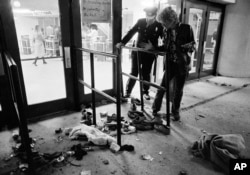 FILE - A security guard and an unidentified man look at an area with shows and clothes strewn around where several people were killed and others injured, as they were caught in a surging crowd entering Cincinnati's Riverfront Coliseum for a Who concert on