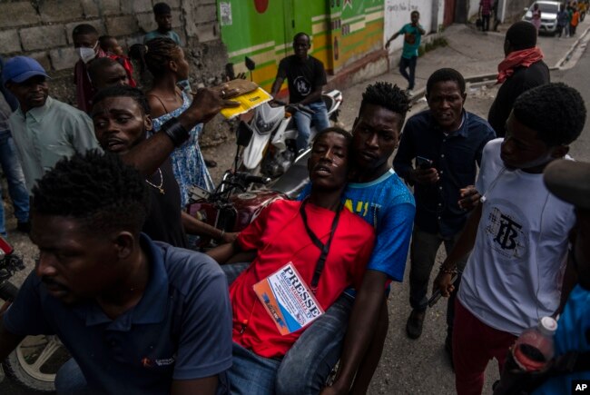 Moun ede yon jounalis ki afekte pa gaz lakrimojen lapolis tire pandan yon manifestasyon kont lanmo jounalis Romelo Vilsaint nan Potoprens, Dimanch 30 Oktob 2022.