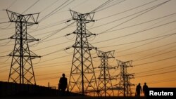 FILE - Locals walk past electricity pylons in Soweto, South Africa, July 3, 2022.