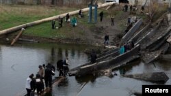 People leave and return to their shelters as they cross a destroyed bridge in order to collect aid in the eastern Donbas region of Bakhmut, Ukraine, Oct. 30, 2022.