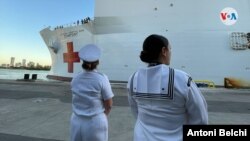 Dos miembros de la Marina de Estados Unidos esperan frente al buque hospital Comfort en el puerto de la ciuda de Miami, Florida, donde partirá hacia varios países de América Latina. Foto: Antoni Belchi / VOA.