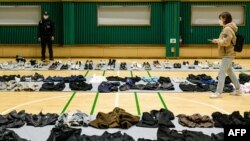 A journalist (R) walks amongst personal belongings retrieved by police from the scene of a fatal Halloween crowd surge that killed more than 150 people in the Itaewon district are displayed at a gymnasium for relatives of victims to collect, in Seoul on November 1, 2022.