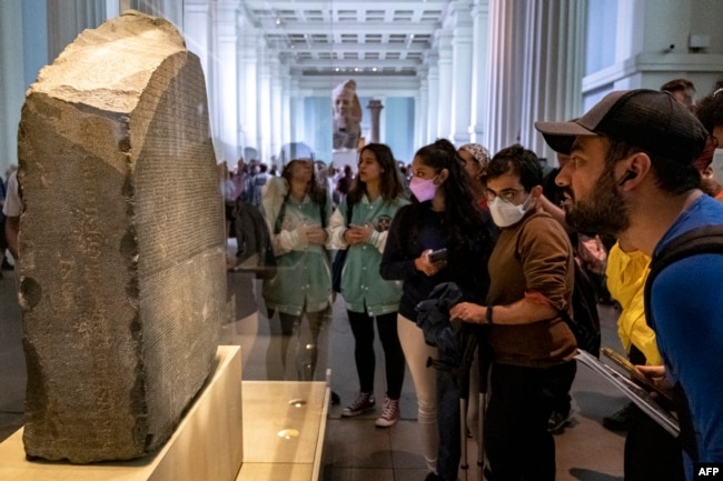 FILE - Visitors view the Rosetta Stone at the British Museum in London on July 26, 2022. (Photo by Amir MAKAR / AFP)