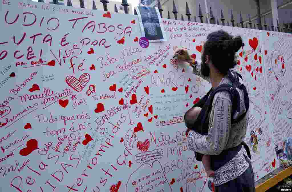 A man writes on a memorial wall in honor of the victims of the COVID-19 at Paulista Avenue in Sao Paulo, Brazil, Oct. 23, 2022.