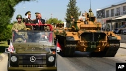 FILE - Turkish Cypriot leader Ersin Tatar, stands on a military vehicle, right, as he reviews the military parade marking the 48th anniversary of the 1974 Turkish invasion in the Turkish occupied area of the divided capital Nicosia, Cyprus, July 20, 2022.