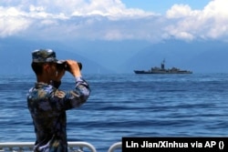 A People's Liberation Army soldier looks through binoculars during military exercises as Taiwan’s frigate Lan Yang is seen in the rear on August 5, 2022. (Lin Jian/Xinhua via AP)