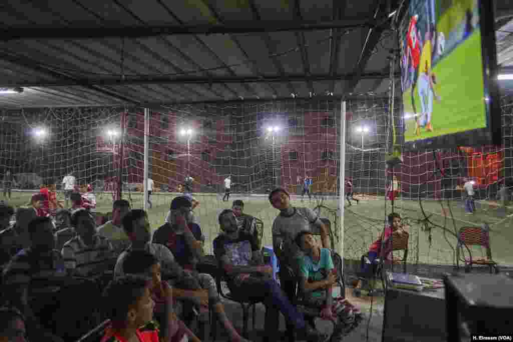 Warga di Kota Nagrig, kampung halaman Mohamed Salah, menyaksikan pertandingan sepak bola di sebuah kafe. Sementara di lapangan sepak bola milik cafe tersebut, sedang berlangsung pertandingan liga sepak bola setempat.