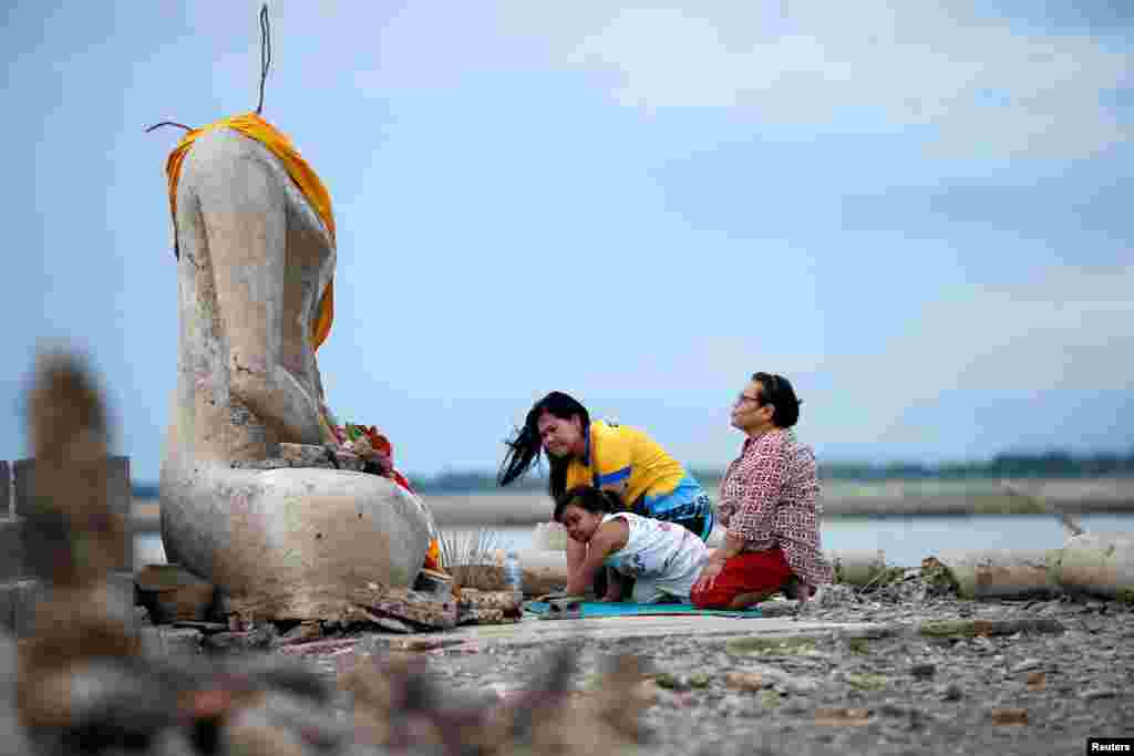 A family prays near the ruins of a headless Buddha statue, which has resurfaced in a dried-up dam due to drought, in Lopburi, Thailand, Aug. 1, 2019.