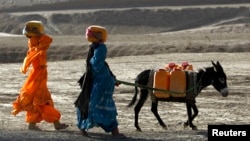 Afghan kochi nomad women carry water containers on their heads as they walk with a donkey outside of Maidan Shar, the capital of Wardak province, Sept. 8, 2013. 