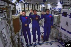 Dalam foto yang dirilis oleh Xinhua News Agency ini, gambar yang diambil dari layar di Pusat Kontrol Dirgantara Beijing menunjukkan astronot China dari kiri, Cai Xuzhe, Chen Dong dan Liu Yang melambaikan tangan dari dalam modul lab Wentian, Senin, 25 Juli 2022. (Guo Zhongzheng/Xinhua via AP)