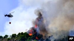 Un helicóptero lanza agua mientras un incendio forestal avanza cerca de una zona residencial en Alhaurín de la Torre, Málaga, España, el sábado 16 de julio de 2022. (AP Foto/Gregorio Marrero)