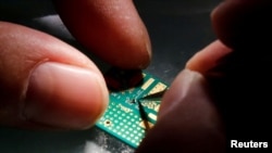 FILE - A researcher plants a semiconductor on an interface board during a research work to design and develop a semiconductor product at Tsinghua Unigroup research center in Beijing, Feb. 29, 2016.