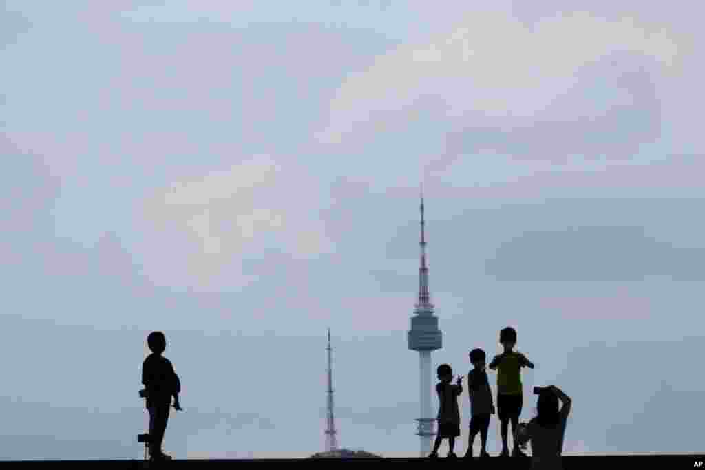 Children posing for a photo are seen silhouetted against the sky and the iconic N Seoul Tower at the National Museum of Korea in Seoul, South Korea.
