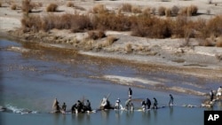 FILE - Afghans try to repair a dam on a river as seen from the British forces forward operating base Sterga II at Helmand province in southern Afghanistan, Dec. 16, 2013.
