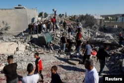 Orang-orang berkumpul di tengah puing-puing rumah penyerang militan Palestina Yahya Mari yang dihancurkan pasukan Israel di Qarawat Bani Hassan di Tepi Barat yang diduduki Israel 26 Juli 2022. REUTERS/Mohamad Torokman