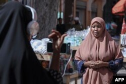 Dua jurnalis perempuan Bilan Media, melaporkan berita dari sebuah pasar di Mogadishu, 22 Mei 2022. (Hasan Ali Elmi / AFP)