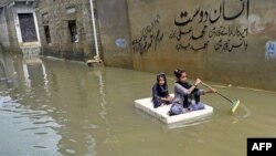 Dua anak perempuan menggunakan rakit untuk melintasi jalanan yang tergenang banjir di daerah permukiman, setelah hujan lebat melanda kota Karachi, Pakistan. (Foto: AFP) 