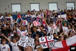 FILE - Young England fans on the stands wave flags before the start of the Women Euro 2022 group A soccer match between England and Norway at Brighton & Hove Community Stadium in Brighton, England, July 11, 2022.