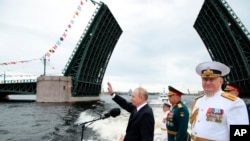 Russian President Vladimir Putin, center, waves as Russian Defense Minister Sergei Shoigu, second right, and Commander-in-Chief of the Russian Navy Admiral Nikolai Yevmenov review warships marking Russian Navy Day in the Gulf of Finland, July 31, 2022.