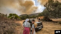 Des évacués observent, impuissants, un feu de forêt qui fait rage près de la ville marocaine de Ksar el-Kebir, dans la région de Larache, le 14 juillet 2022.