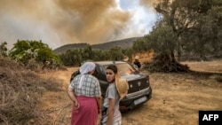 FILE: Evacuated people look on as they stand next to a vehicle while behind a wild forest fire rages near the Moroccan city of Ksar el-Kebir in the Larache region. Taken 7.14.2022