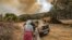 FILE: Evacuated people look on as they stand next to a vehicle while behind a wild forest fire rages near the Moroccan city of Ksar el-Kebir in the Larache region. Taken 7.14.2022