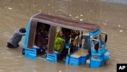 A rickshaw driver and a volunteer push a rickshaw stuck in a flooded road after a heavy rainfall in Karachi, Pakistan, July 11, 2022.