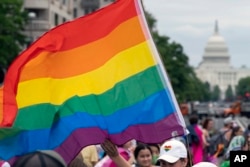 FILE - With the US Capitol in the background, a person waves a rainbow flag as they participant in a rally in support of the LGBTQIA+ community at Freedom Plaza, June 12, 2021, in Washington.