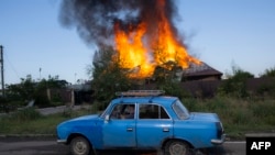 A Ukrainien man drives past a burning house hit by a shell in the outskirts of Bakhmut, eastern Ukraine, July 27, 2022, amid the Russian invasion of Ukraine. 