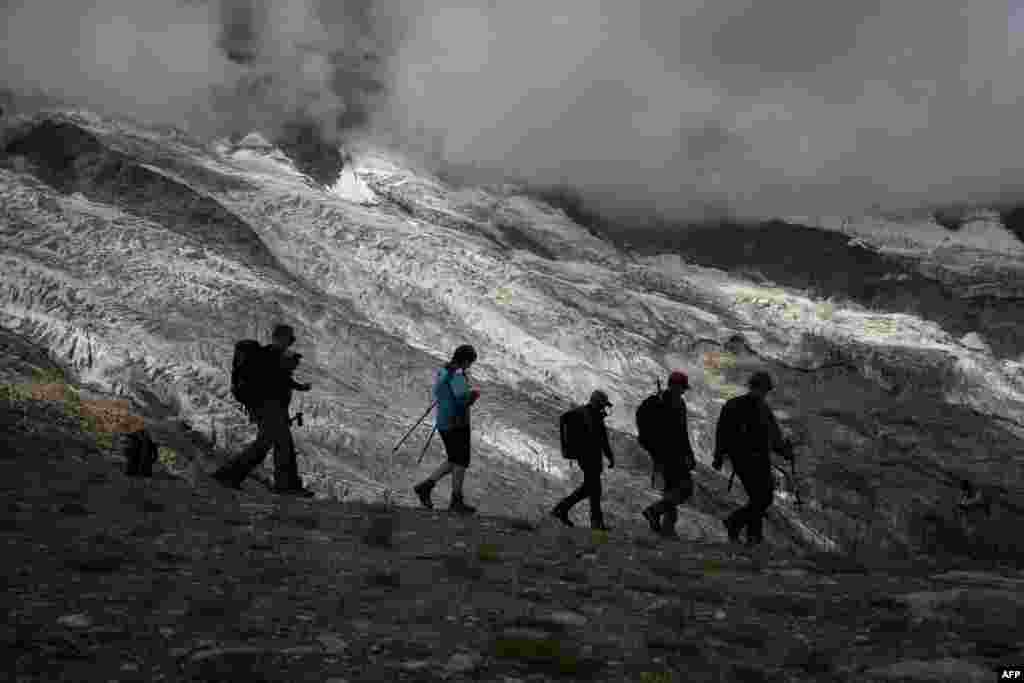 Hikers are seen in silhouette walking next to the Fee Glacier above the Swiss alpine resort of Saas-Fee, Switzerland, July 30, 2022.