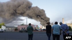 Orang-orang memperhatikan asap yang membubung dari serangan misil ke sebuah gudang milik perusahaan perdagangan di Odessa, 16 Juli 2022 di tengah invasi Rusia ke Ukraina. (Foto: Oleksandr Gimanov/ AFP)