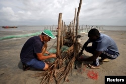 Volunteers, Gilbert Bassene, 37, a primary school teacher, and Patrick Chevalier, 69, a retired economist work on an erosion barrier during low tide in Diogue island, Senegal July 14, 2022. (REUTERS/Zohra Bensemra)