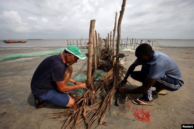 Volunteers, Gilbert Bassene, 37, a primary school teacher, and Patrick Chevalier, 69, a retired economist work on an erosion barrier during low tide in Diogue island, Senegal July 14, 2022. (REUTERS/Zohra Bensemra)