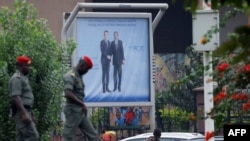 Pedestrians walk past a poster displaying Cameroonian President Paul Biya (R) next to his French counterpart Emmanuel Macron, in a street in Yaounde on July 25, 2022, prior to the French president's visit. 