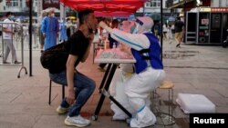 A medical worker, wearing a protective suit and straddling an ice block, collects a swab from a resident at a nucleic acid testing site amid a heat wave warning, following a COVID-19 outbreak in Shanghai, China, July 12, 2022.