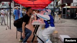 A medical worker, wearing a protective suit and straddling an ice block, collects a swab from a resident at a nucleic acid testing site amid a heat wave warning, following a COVID-19 outbreak in Shanghai, China, July 12, 2022.