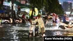 ស្រ្តី​ម្នាក់​កំពុង​បណ្តើរ​ម៉ូតូ​ដែល​ខូច​ដោយសារ​ទឹក​លិច​ ​លើ​បណ្តោយ​ផ្លូវ​ហ្សាល​ដឺហ្គោល រាជធានី​ភ្នំពេញ​ នៅ​ថ្ងៃទី២៣ ខែ​មិថុនា ឆ្នាំ​២០២២។ (កាន់ វិច្ឆិកា/វីអូអេ)