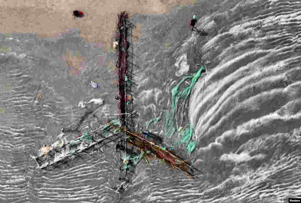 An aerial view shows volunteers, Gilbert Bassene, 37, a primary school teacher, and Patrick Chevalier, 69, a retired economist, working on the wooden Gryones using the Maltais-Savard Ears System to hold back sediments and counter the erosion of the shoreline during low tide in Diogue island, Senegal.