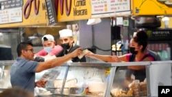 Money is exchanged at a food stand while workers wear face masks inside Grand Central Market, July 13, 2022, in Los Angeles. Los Angeles County might be imposing a mask-wearing mandate later this month if COVID-19 numbers continue to rise.