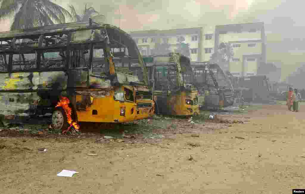 People walk past damaged school buses that were set on fire by a mob in the school campus after a female student&#39;s death in Kallakurichi district in the southern state of Tamil Nadu, India.