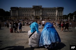 People sit covering their heads from the sun after a scaled down version of the Changing of the Guard ceremony took place outside Buckingham Palace, during hot weather in London, Monday, July 18, 2022. (AP Photo/Matt Dunham)